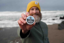 Man holding a container of beard balm on a beach