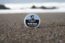 Beard balm container on a beach with ocean in the background