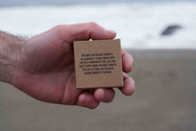 Hand holding a small cardboard box with text on a blurred beach background
