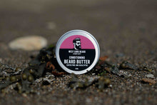A round tin of West Cork Beard Company Conditioning Beard Butter standing upright on a textured, dark seaweed and moss surface.