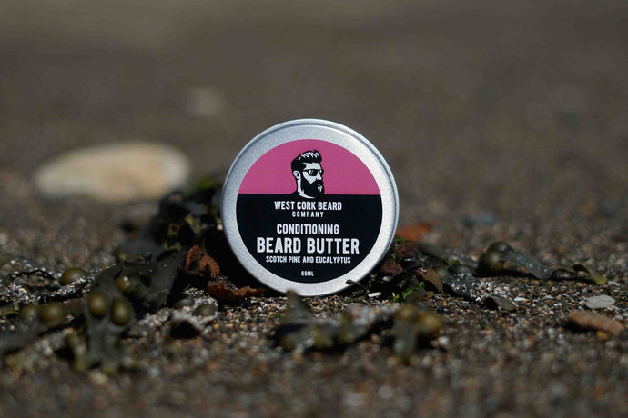 A round tin of West Cork Beard Company Conditioning Beard Butter standing upright on a textured, dark seaweed and moss surface.